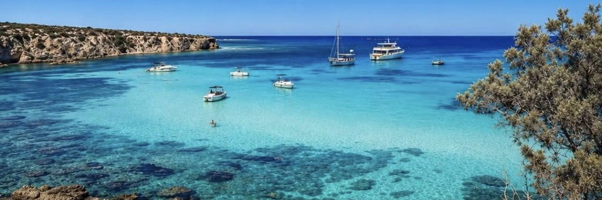 Türkisblaue Bucht mit ankernden Booten und Felsküste