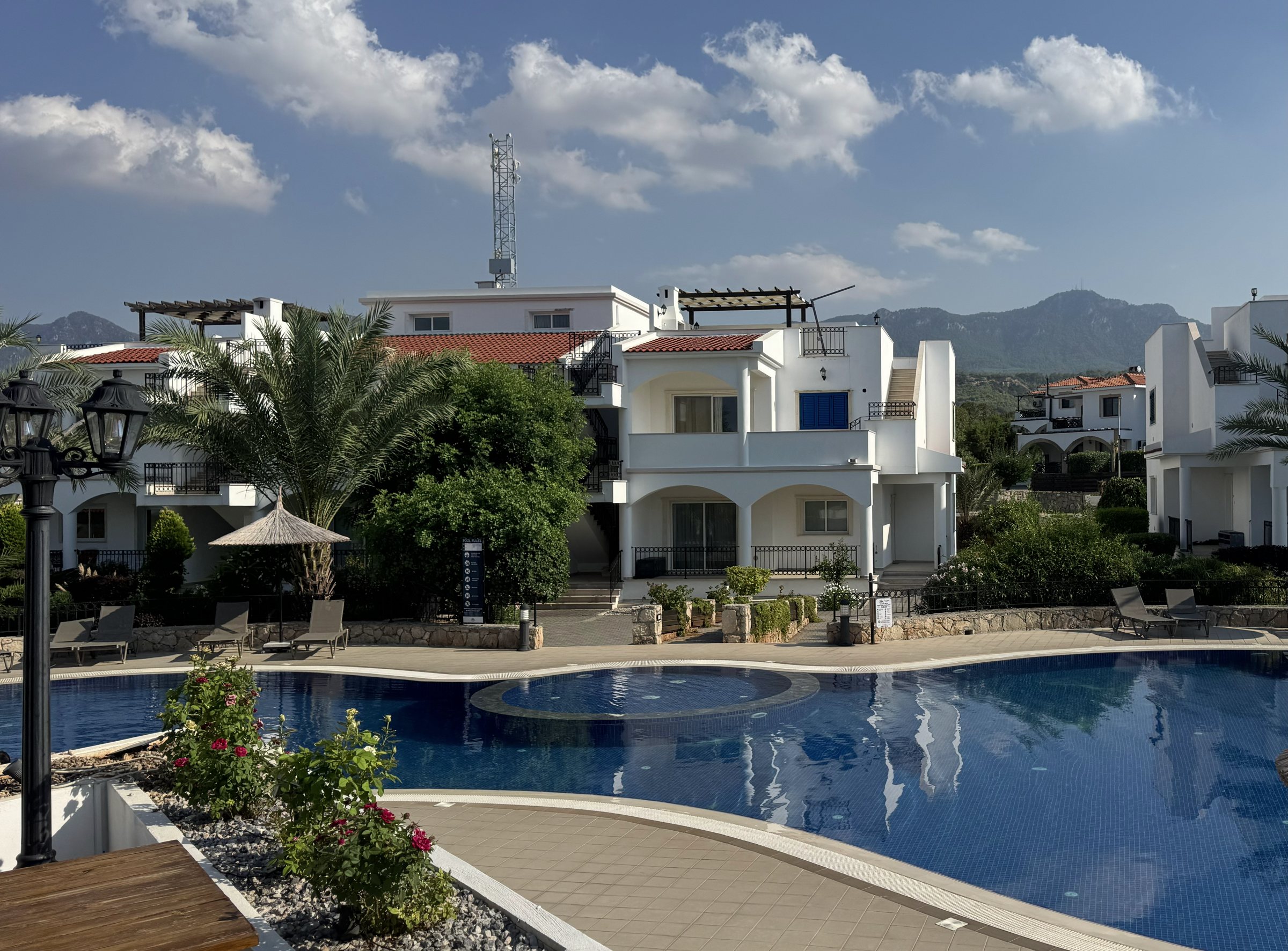 Ferienanlage in Esentepe mit weißen Häusern, Palmen und großem Pool vor dem Kyrenia-Gebirge