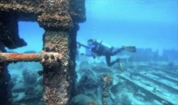 Taucher erkundet ein bewachsenes Wrack unter Wasser