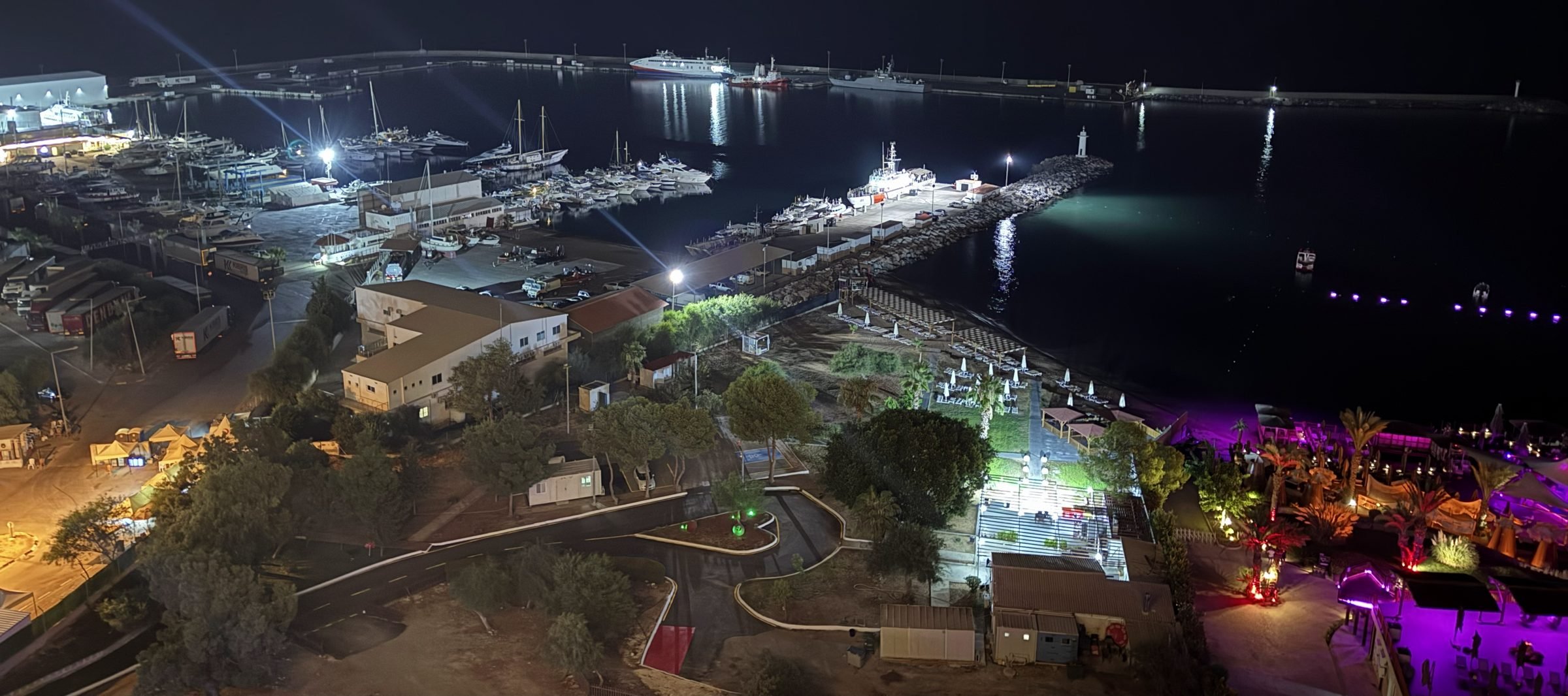 Luftaufnahme des beleuchteten Hafens bei Nacht mit Jachten, Mole und Strand