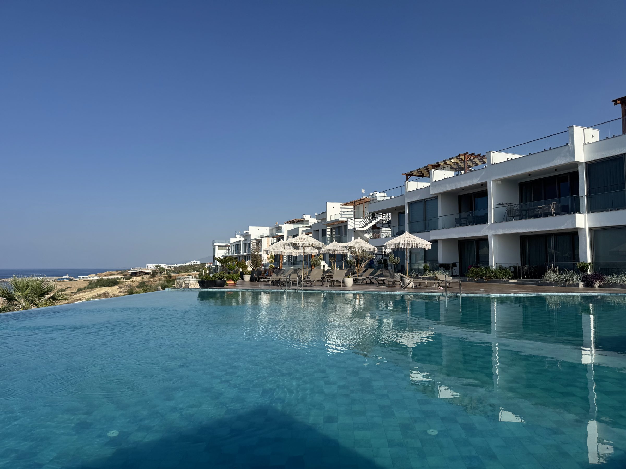 Weiße Studio-Anlage mit Infinity-Pool, Sonnenschirmen und Blick aufs Meer in Esentepe